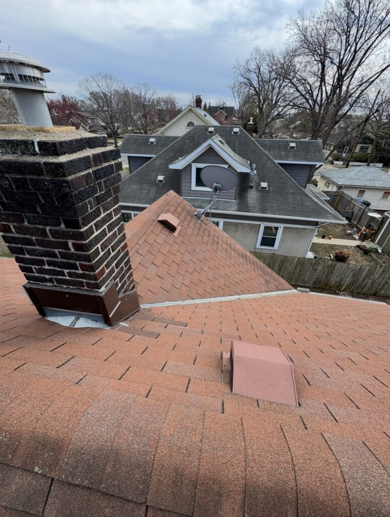 an old roof with a roof cricket located above the chimney to divert water around the chimney