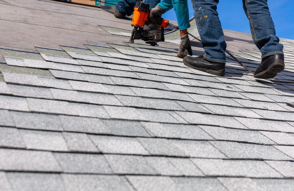roofer installing roof shingles with pnuematic roofing nailer.