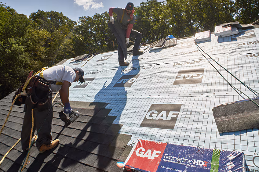 a roof getting installed by roofing crew and a bundle of shingles laying on the roof