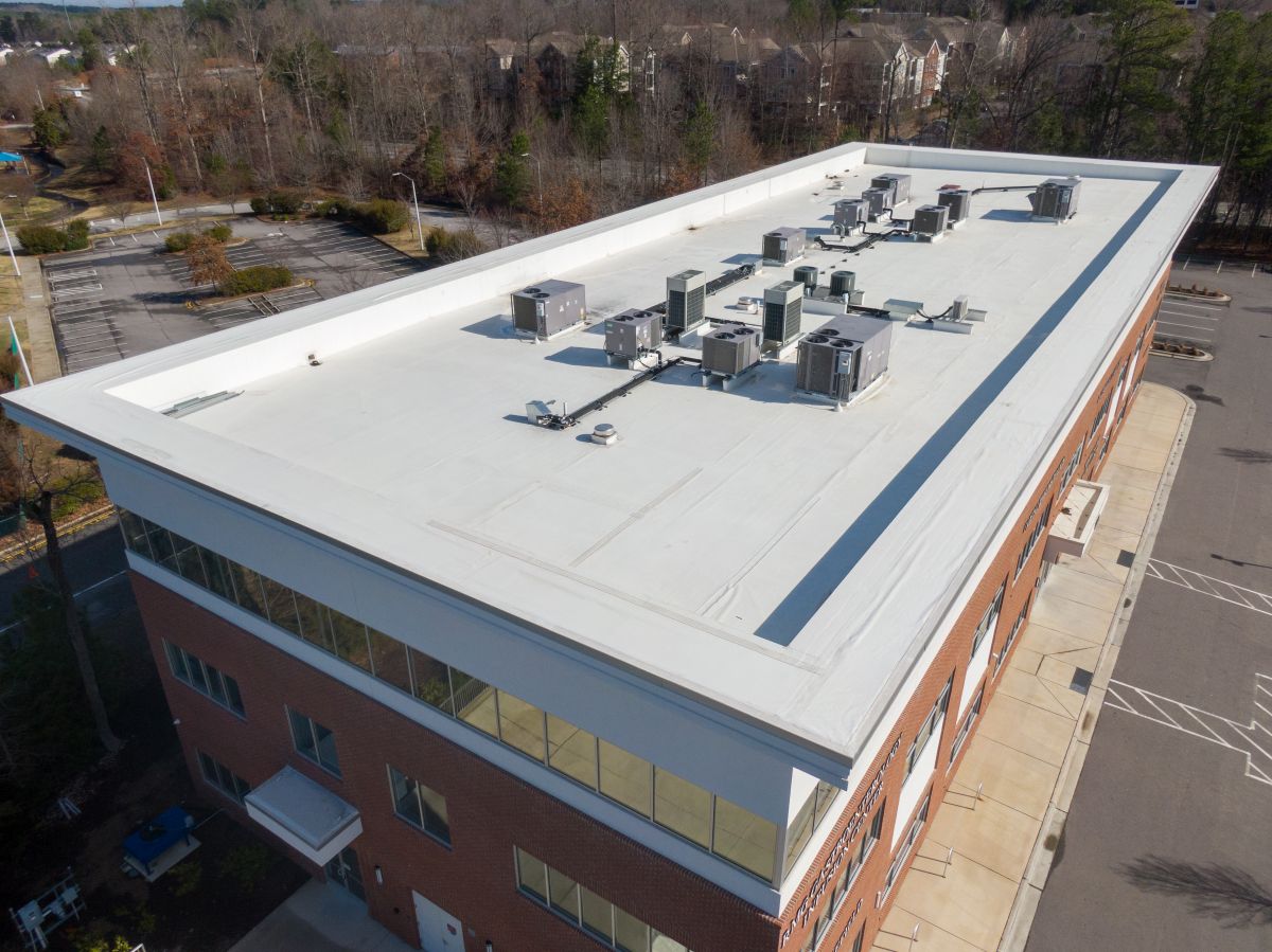 white flat commercial roof with trees in the background