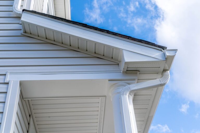 Classic white gutter system that collects water shedding off the roof, with slip connector, end cap, elbow tube, gutter hanger, gutter drop connecting the outlet to the downspout with soffit, fascia