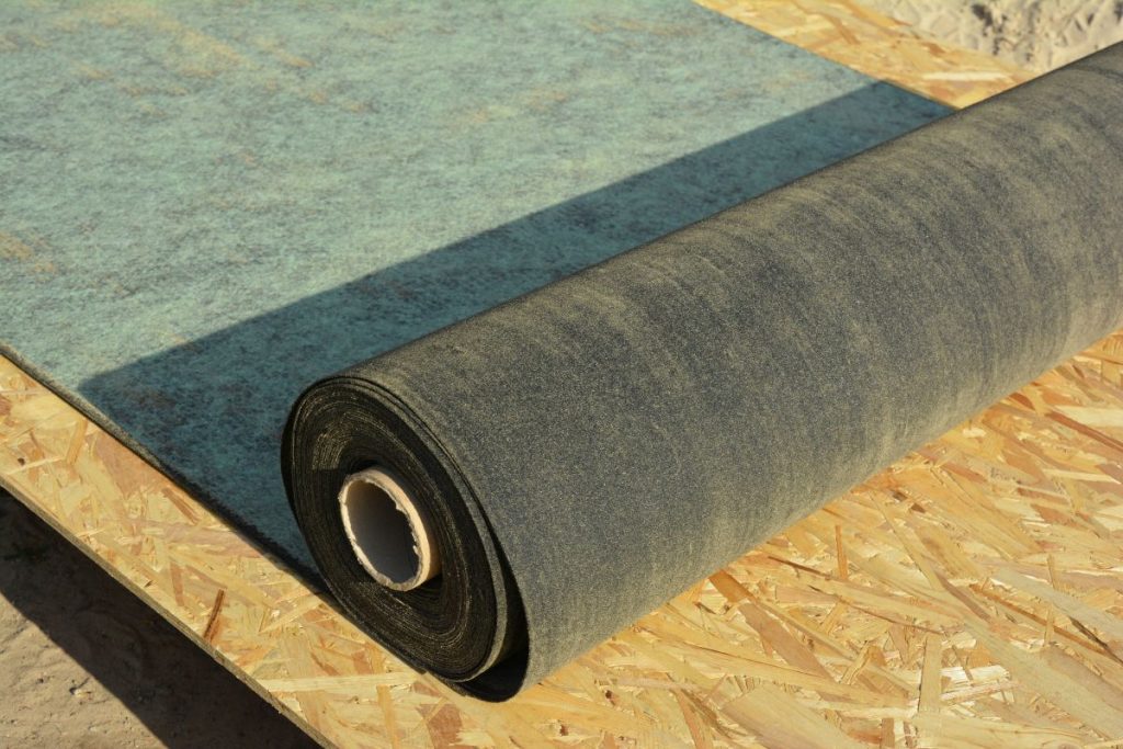 Unrolling waterproofing, water-resistant felt, bituminous roofing underlayment on the roof sheathing 