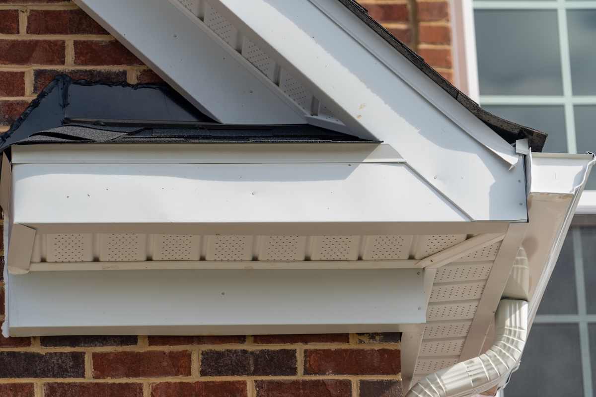 Gable with brick and vinyl siding, white frame gutter guard system, fascia, drip edge, soffit, on a pitched roof attic at a luxury American single family home neighborhood USA