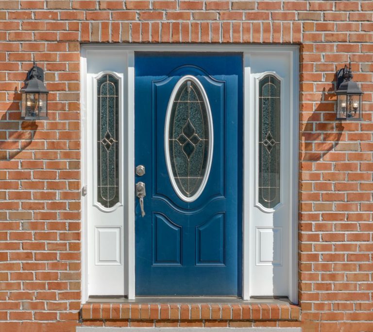 Close up view of elegant blue wooden door with oval stained window, with white sidelights,
